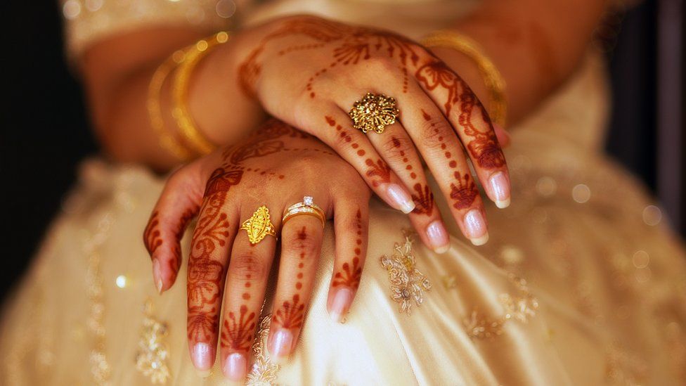 A bride is sitting with her hand covered in henna