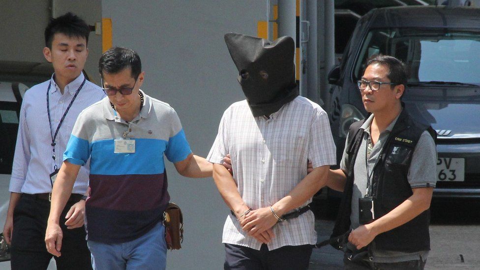 Khaw Kim-sun, wearing a black hood over his face, being escorted by police at Ma On Shan Police Station in Hong Kong