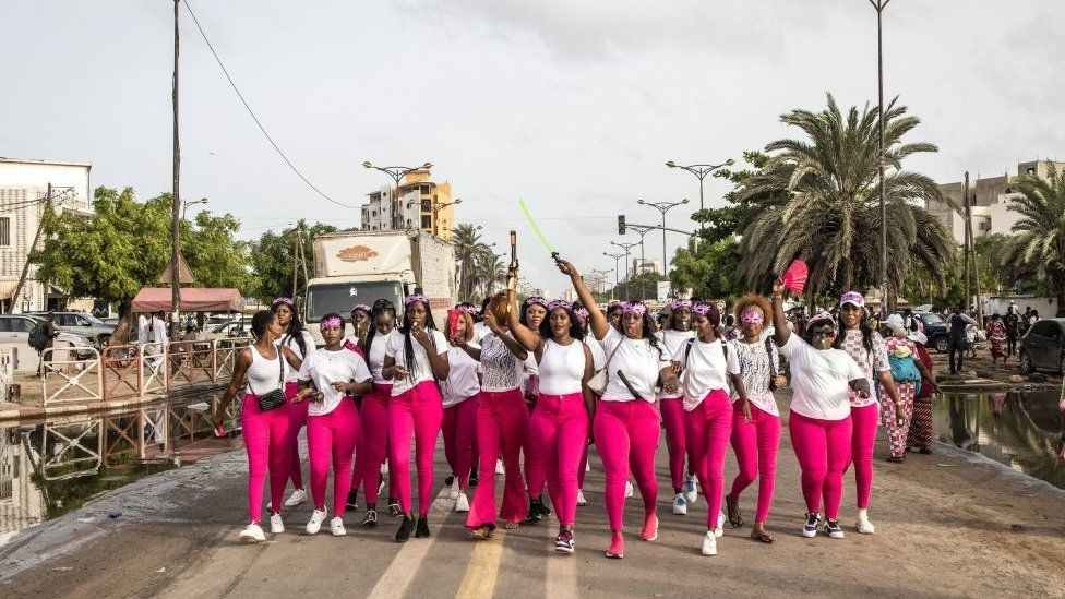 A group of women standing on the streets of Senegal wearing pink leggings and white tops.