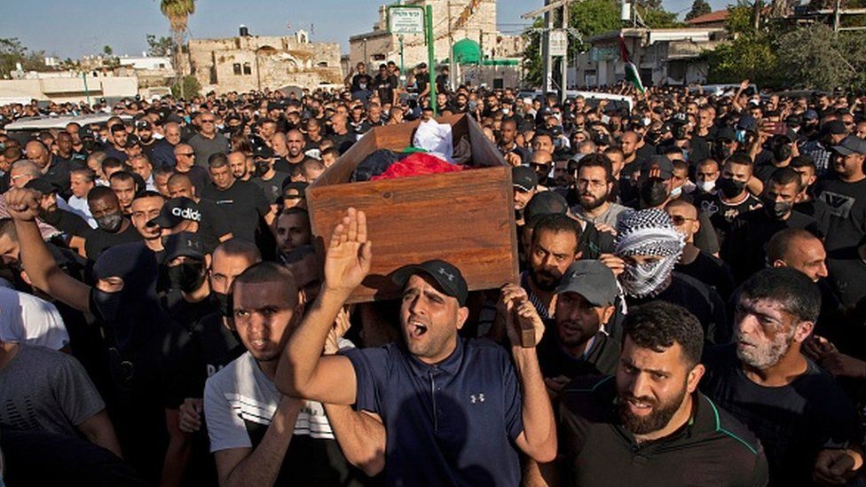 Arab Israelis gesture and wave Palestinian flags during a funeral in the central Israeli city of Lod near Tel Aviv