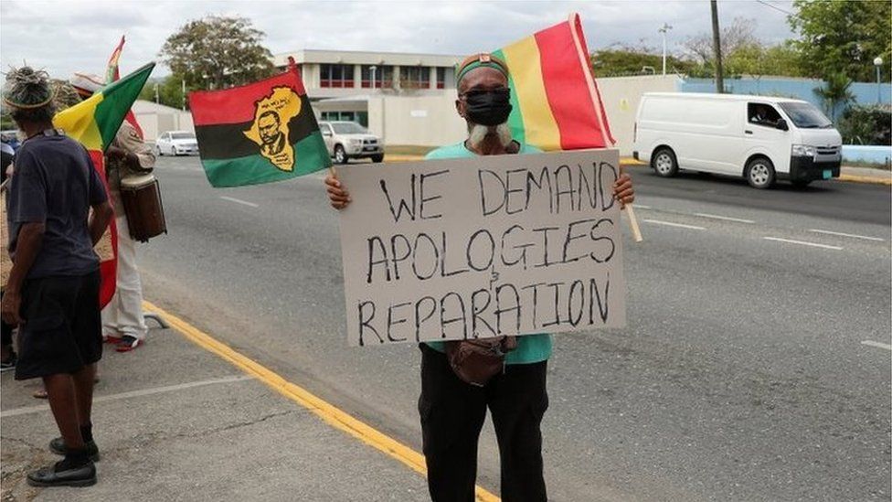 Протестующий держит плакат во время митинга с требованием возмещения ущерба Соединенному Королевству за рабство в преддверии визита на Ямайку герцога и герцогини де Кембридж в рамках их тура по Карибскому морю, за пределами Британской Верховной комиссии, в Кингстоне, Ямайка, 22 марта 2022 г.