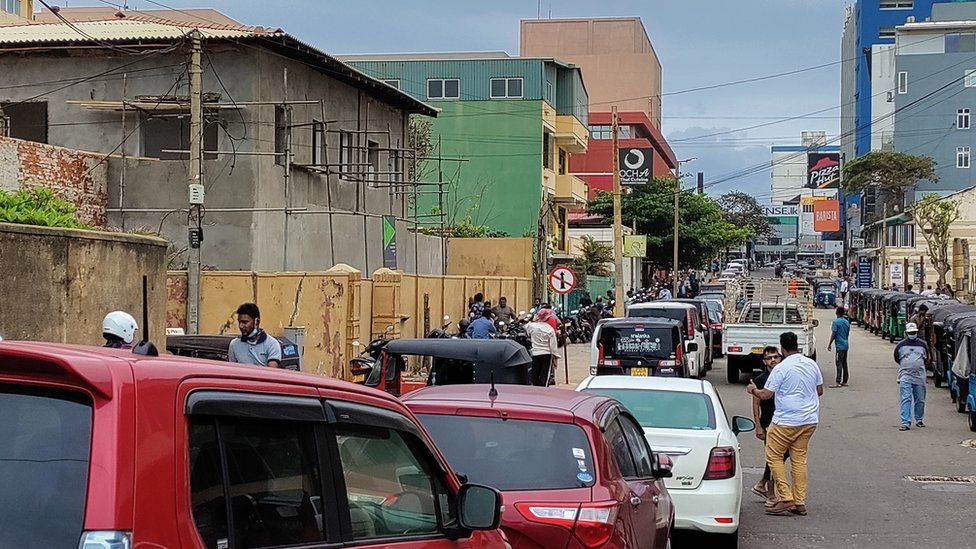 A street sloping upwards is filled with cars in single file stretching as far as the eye can see.