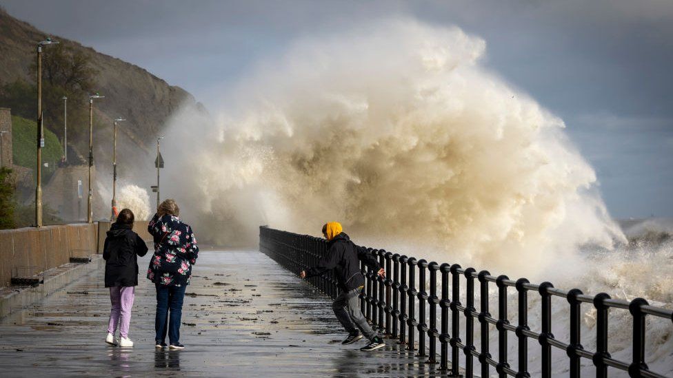 People walking in Folkestone while waves created by Storm Ciarán crash into the promenade