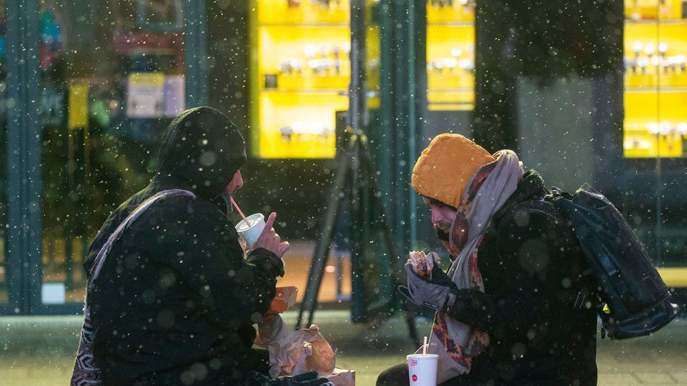 Люди едят, когда идет снег во время зимнего шторма на Таймс-сквер в Нью-Йорке