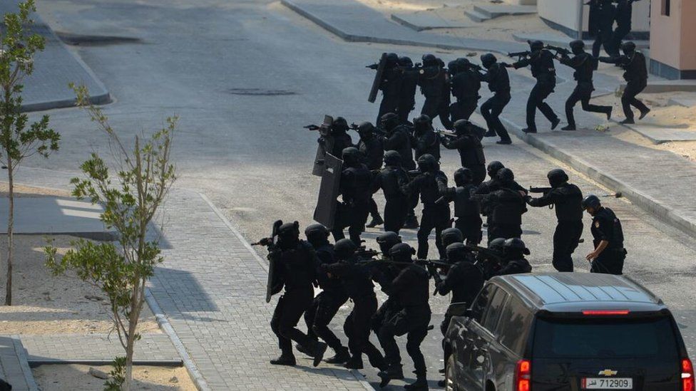 Security forces dressed in black cross a road in preparation for a practice raid