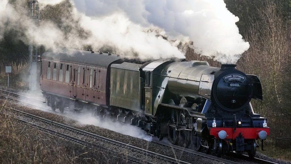 Steam train running on a line with smoke coming from the boiler. Flying Scotsman nameplate.
