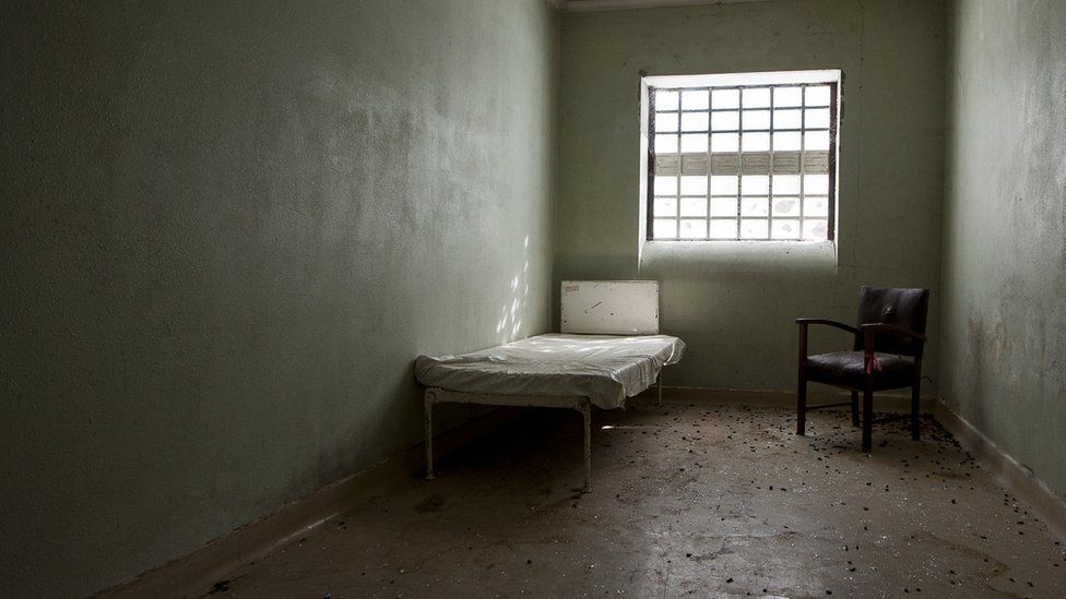 The photo shows an empty room featuring a bed and a chair in a corner
