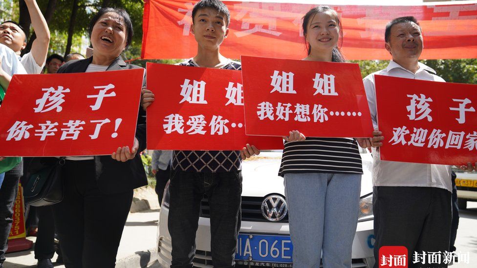 Kang Ying's family hold up placards to greet her