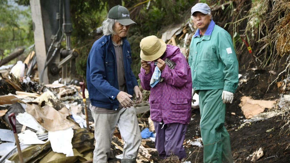 Residents of Atsuma standing next a collapsed house