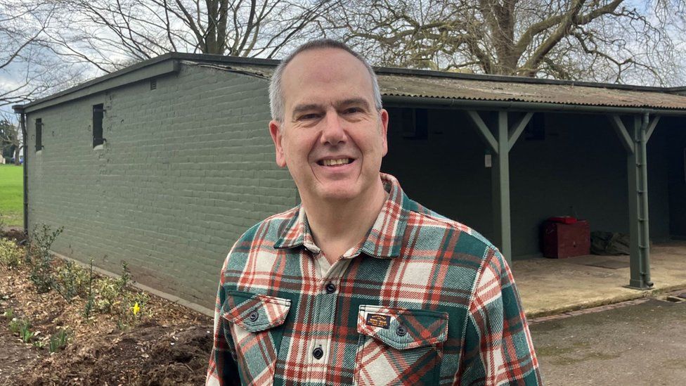 Julian Tooke wearing a checked shirt smiling near a large shed