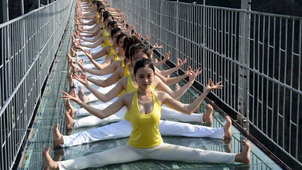 Women practice yoga during a performance on the Brave Man's Bridge glass bridge in Shiniuzhai, Pingjiang county, Hunan province