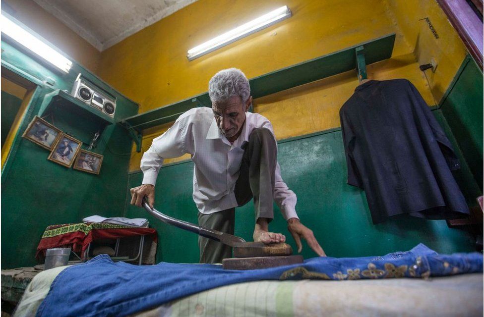 A man with his foot on an appliance as he heats up his iron.
