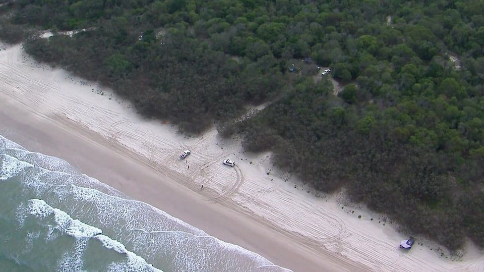 An aerial view of 4x4 vehicles and a few people on a beach next to bushland on Bribie Island