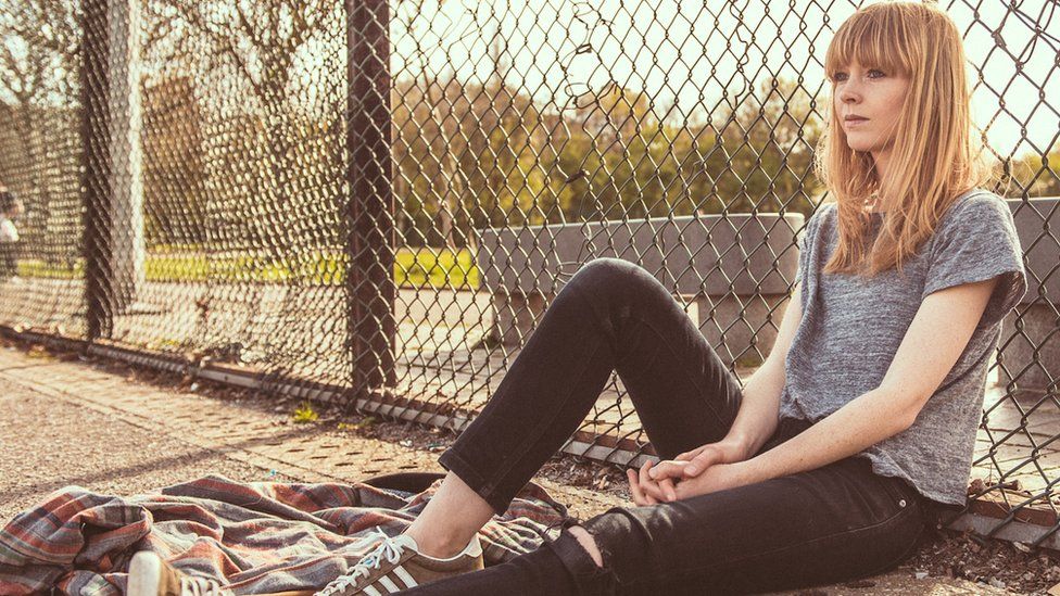 Lucy Rose sitting by a fence