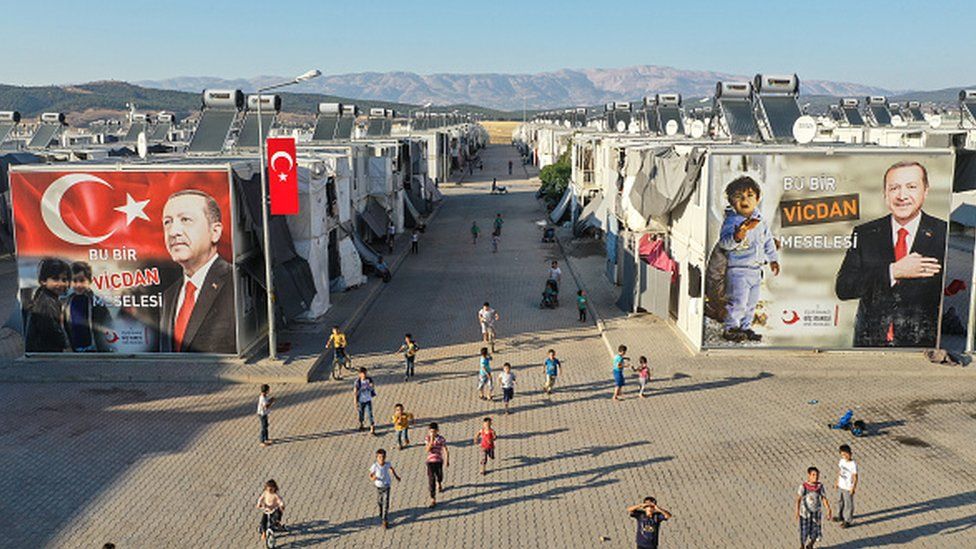 Syrian refugee children play in front of a poster of Turkey's president at a refugee camp in Kahramanmaras, Turkey