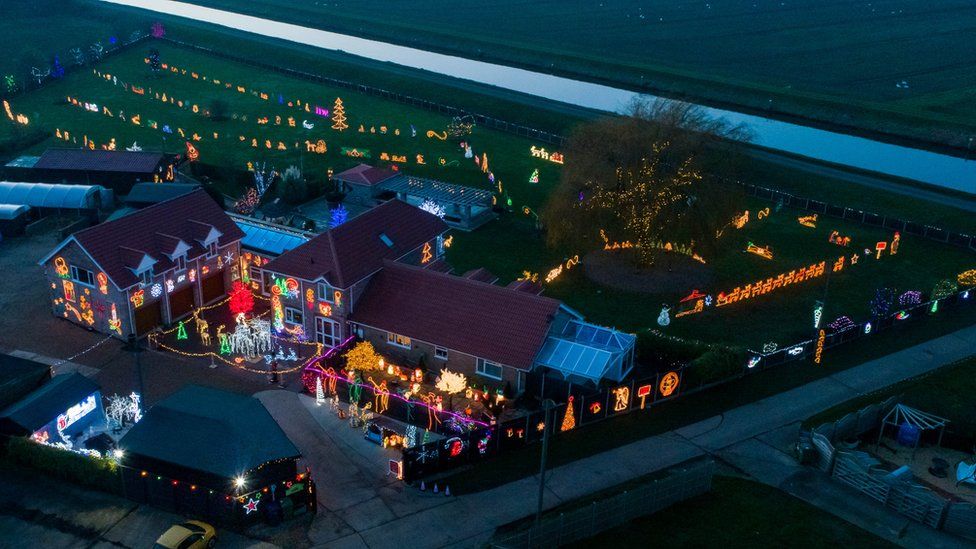 An aerial shot of a house and garden heavily decorated with Christmas lights and illuminated models.