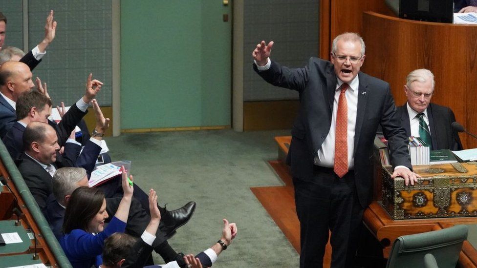 Australian Prime Minister Scott Morrison and several government MPs raise their hands in the House of Representatives