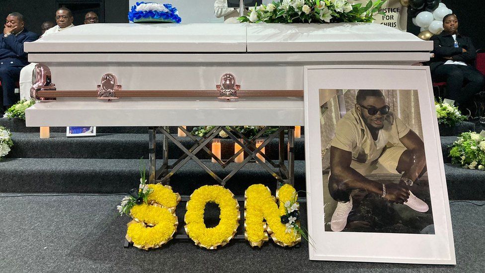 Chris Kaba's coffin with a floral tribute saying "son" next to a framed photograph of him