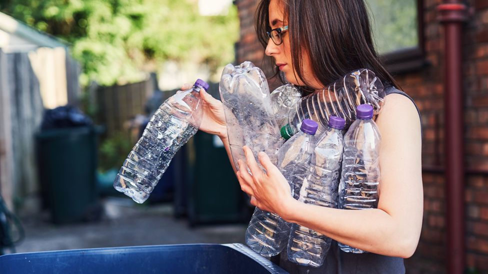 Stock image of a woman putting plastic bottles into a recycling bin