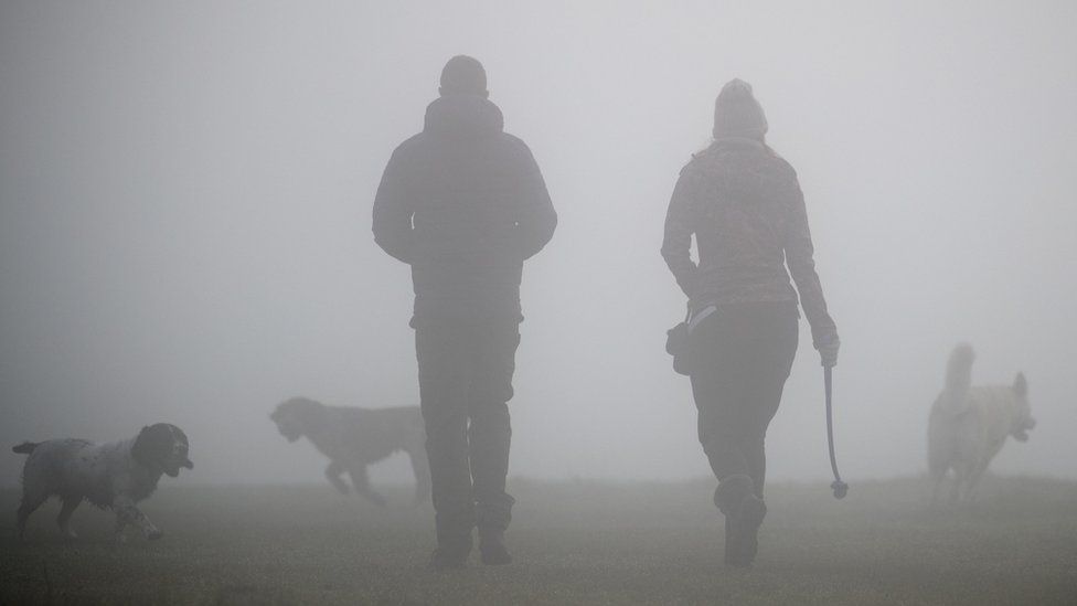 People walk their dogs through thick fog on Basingstoke Common near to Old Basing, Hampshire.