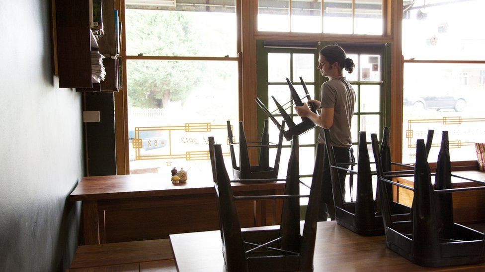 A cafe worker puts chairs on top of tables in an empty cafe