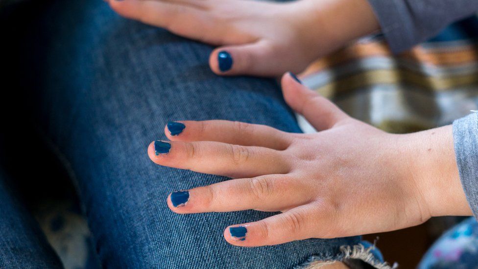 A young girl with a blue nail polish manicure