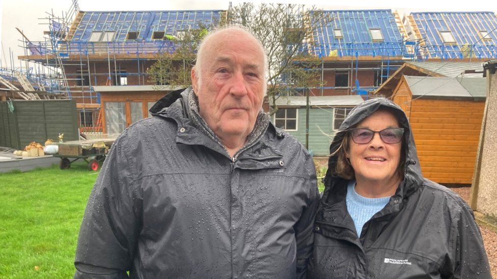 Mr and Mrs King standing in their garden with the new builds behind them