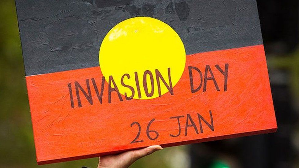A protester holds a message written on an Aboriginal flag saying: "Invasion Day 26 Jan"