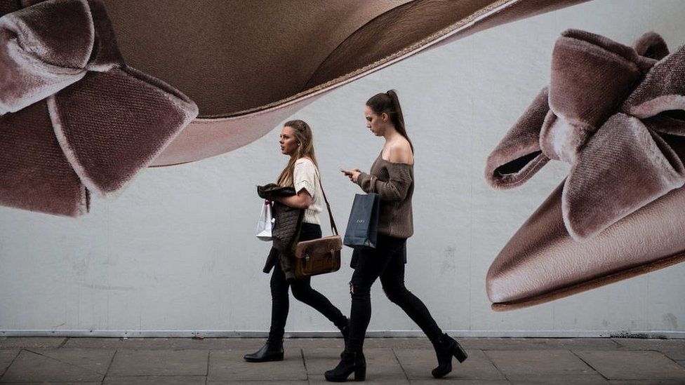 Two women walk past a large board advertising shoes on Oxford Street in London on April 28, 2017