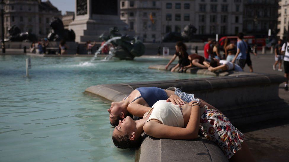 Two women dip their heads into the fountain to cool off in Trafalgar Square
