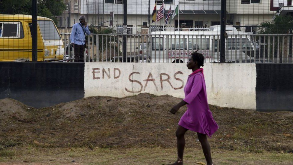 A pedestrian walks past a road divider adorned with EndSars graffiti