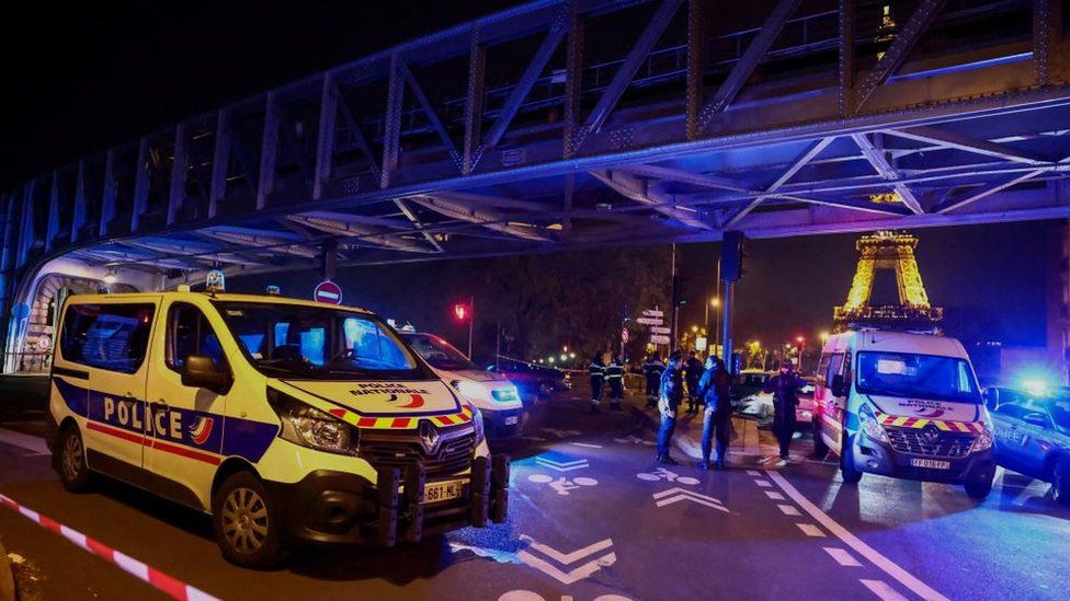 Scene showing emergency vehicles and lit-up Eiffel Tower in background