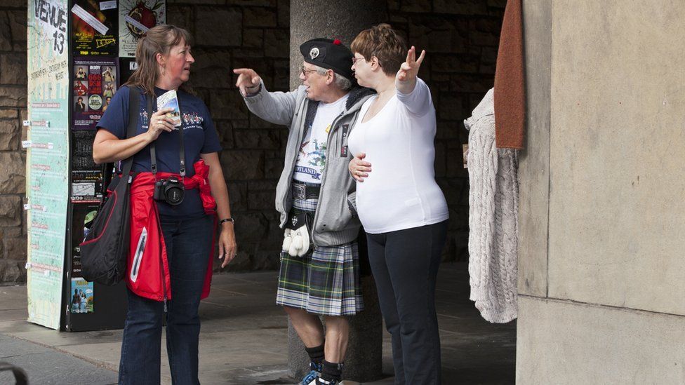 EDINBURGH, SCOTLAND, GREAT BRITAIN - AUGUST 13: Owners of a shop targeted at tourists give directions to a visitor during the Edinburgh festival, on August 13, 2014