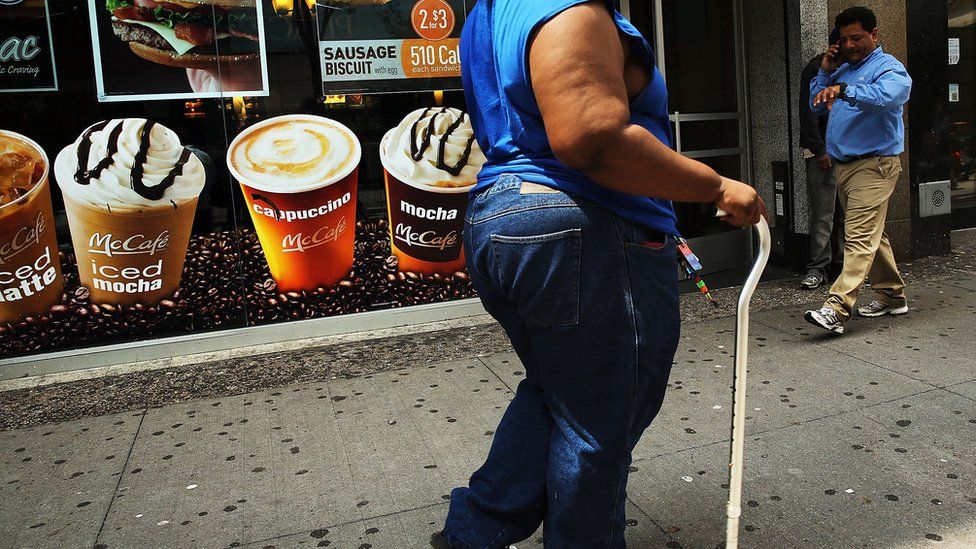 Overweight person walks past sign advertising sugary drinks