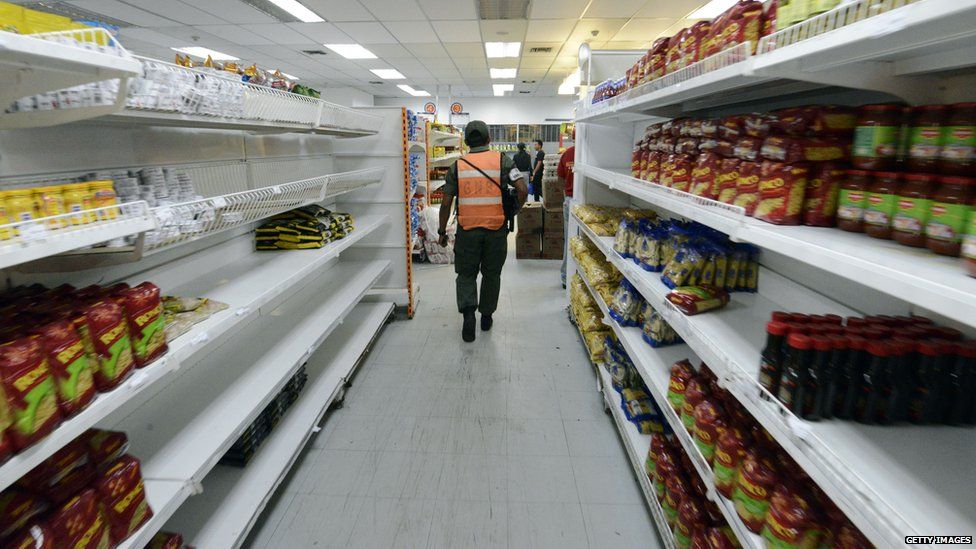 Member of the national guard patrolling a supermarket aisle with many empty shelves