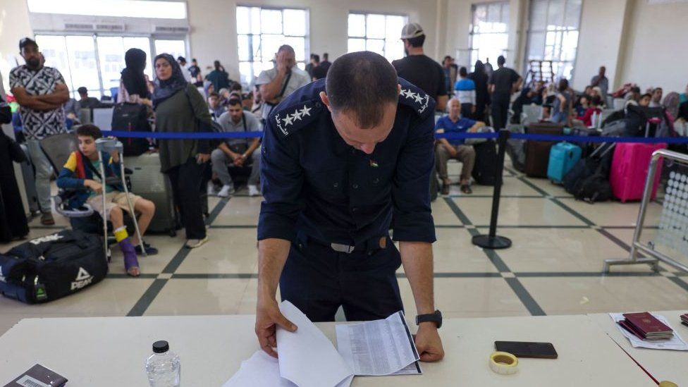 A Palestinian border guard checks the documents of dual nationals and foreigners as they wait to cross the Rafah border crossing with Egypt, in the southern Gaza Strip, on November 7, 2023,