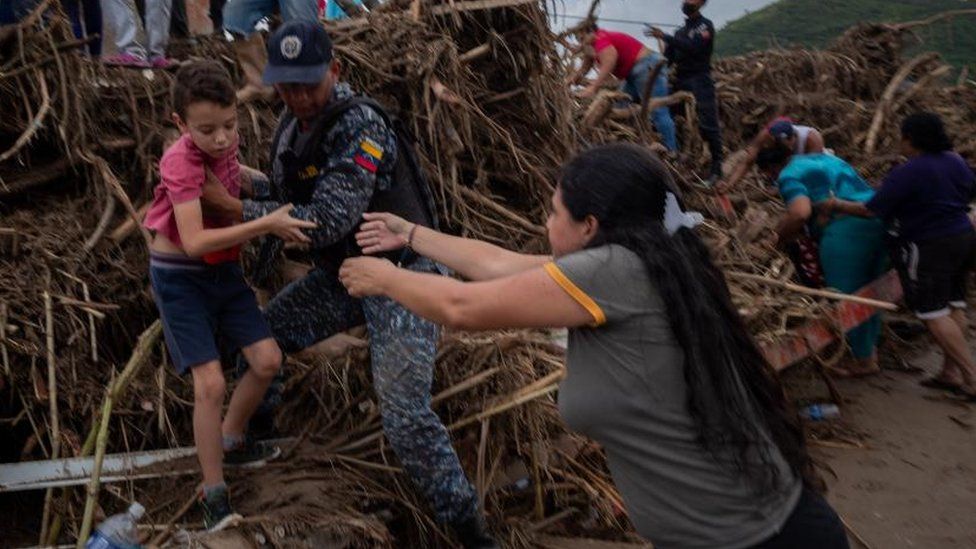 A member of a rescue service aids a child amid damage left by flooding of the Los Patos river, in Tejerias, Aragua state, Venezuela, 09 October 2022.