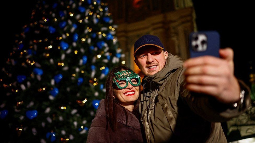 A couple takes a selfie next to a Christmas tree during a celebration the New Year's eve, amid Russia's attack on Ukraine, in front of the St. Sophia Cathedral in Kyiv, Ukraine December 31, 2023.
