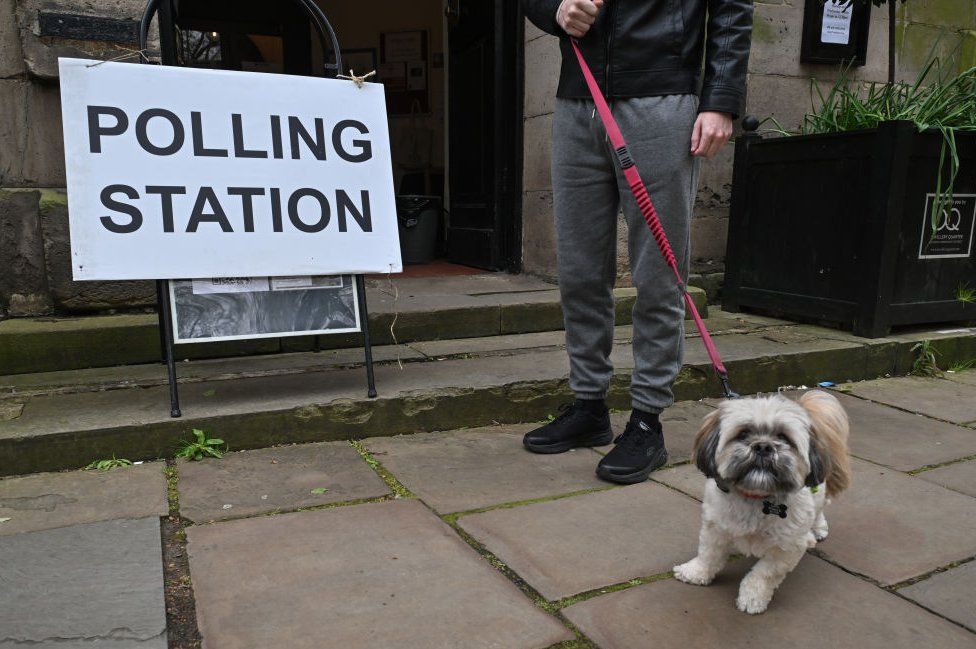 A man holds a dog on a lead as members of the public arrive to vote at a polling station at St. Paul's church in the Jewellery Quarter on May 02, 2024 in Birmingham, England