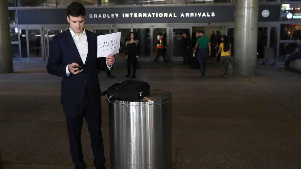 A lawyer holds a sign offering his services to those affected by President Trump's immigration order, at Los Angeles International Airport