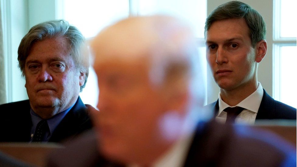 Behind an out of focus figure, Steve Bannon and Jared Kushner are pictured staring almost into lense of camera