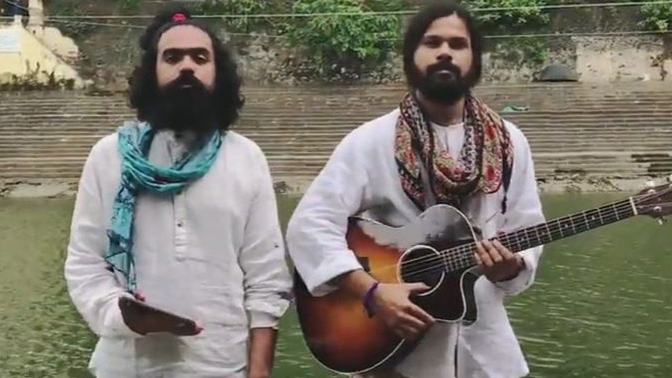 A screengrab from the video shows two bearded male musicians, one holding a guitar