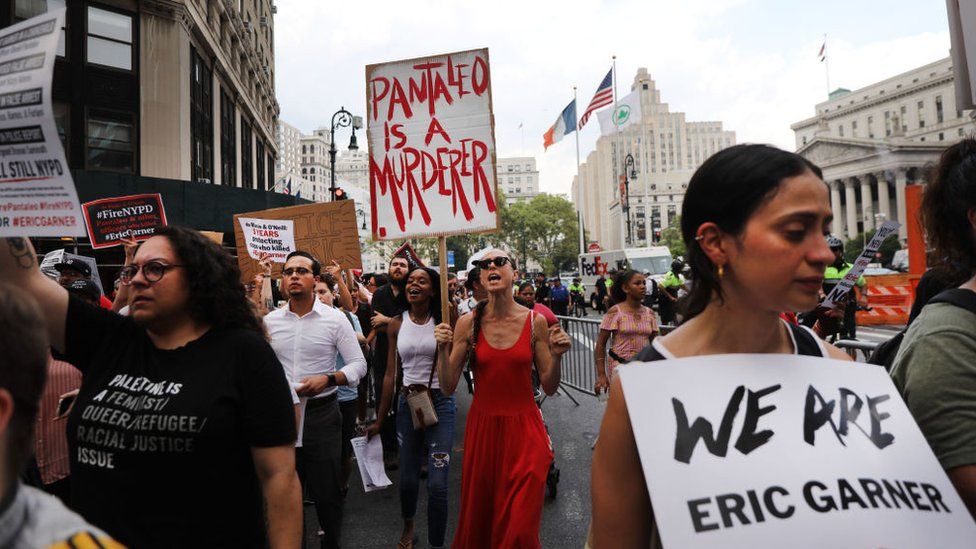 Protesters hold signs, including one that reads "Pantaleo is a murderer"