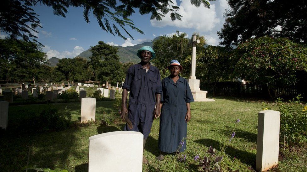 Shadrack Paull and Lusia Axalte stand holding hands among the graves at the cemetery in Tanzania