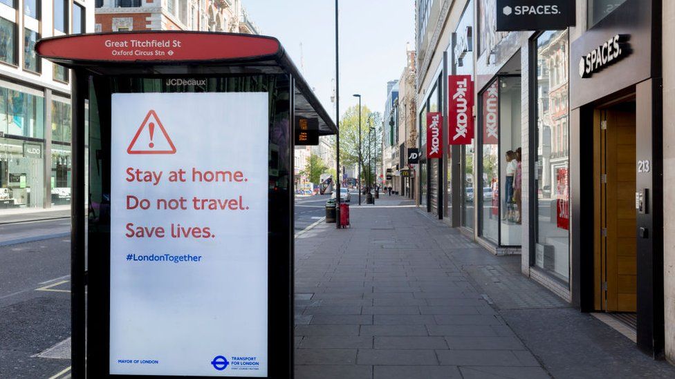 Deserted Oxford Street in London, and a bus shelter sign warning shoppers to stay home
