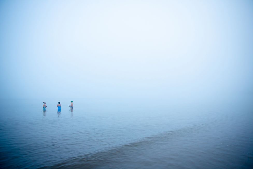 Swimmers in the Mist - three distant people standing in the sea, surrounded by dense mist