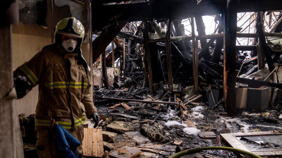 A firefighter stands inside a charred room