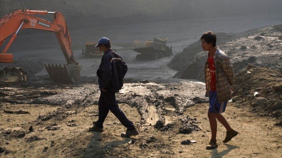 Two men walk past the "mud lake" caused by the landslide in Kachin, with vehicles emerging from the mud