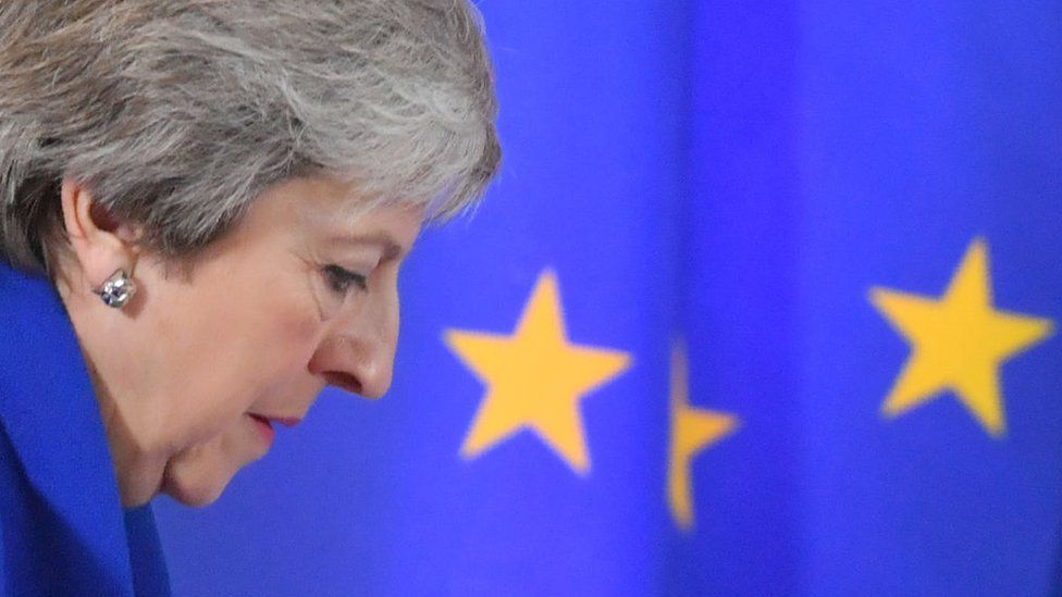 Theresa May stands in front of the EU flag