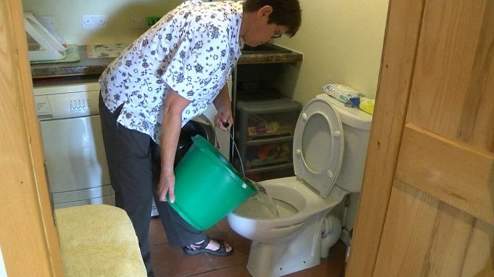 Helen Rees puts a bucket of water into the toilet